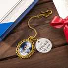 A gold graduation hat tassel ornament with a photo of an older woman and a charm that reads "so PROUD of you," placed next to a diploma and a red ribbon.