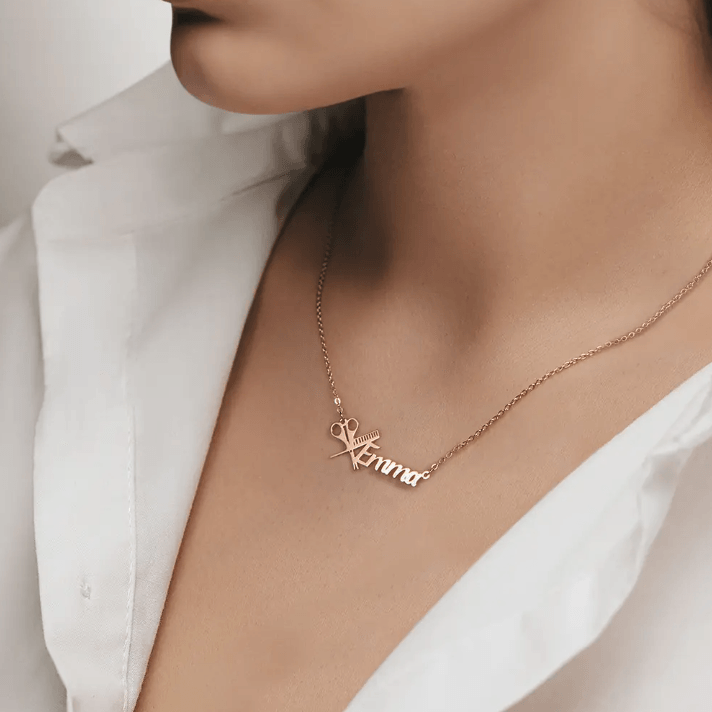 Rose gold personalized hairdresser necklace with the name Emma, featuring a scissors and comb design, worn by a woman in a white shirt.