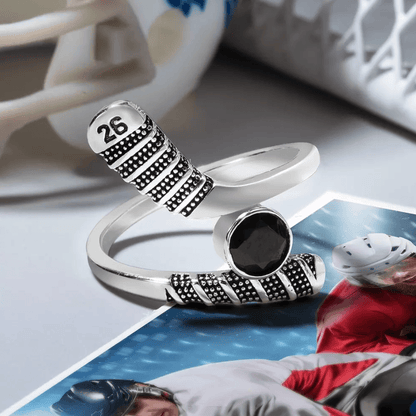 Silver hockey stick ring with black gemstone and '26' detail, placed over an action-packed hockey game photo.