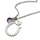 Personalized silver horseshoe necklace with engraved initial disc and purple birthstone charm, symbolizing luck and protection, on a white background.