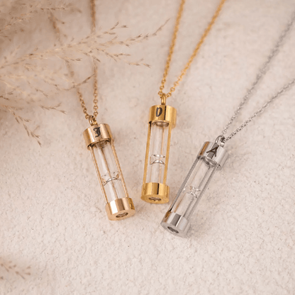 Three hourglass urn necklaces in gold, rose gold, and silver, each with a personalized initial on a soft background.