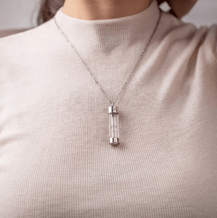 Close-up of a silver hourglass urn necklace worn by a woman in a light sweater, showcasing minimalist elegance.