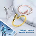 Three customizable hockey stick-shaped rings in silver, gold, and rose gold, featuring letters, numbers, and heart icons, with a hockey player image on the side.