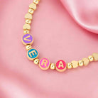Close-up of personalized name necklace with colorful enamel letters and gold beads