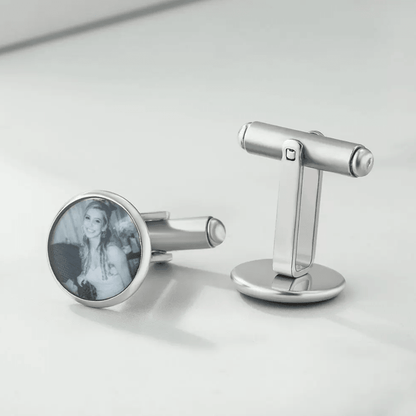 Silver cufflinks on a white surface, one featuring a black and white photo of a smiling woman.