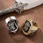 Two men's flip rings displayed on leather, one in silver with black accents and one in gold, beside an ornate feather quill.