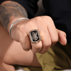 Man's fist showcasing a gold flip ring with intricate double initials design against a tattooed forearm.