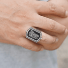 Close-up of a man's hand wearing a silver flip ring with embossed double initials on a black background.