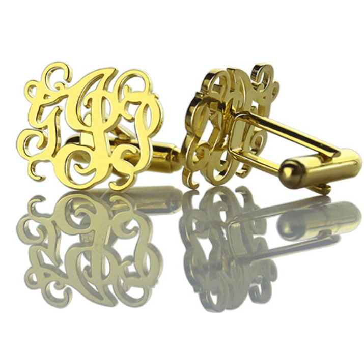 Gold monogram cufflinks with intricate script design, reflecting elegantly on a shiny surface.