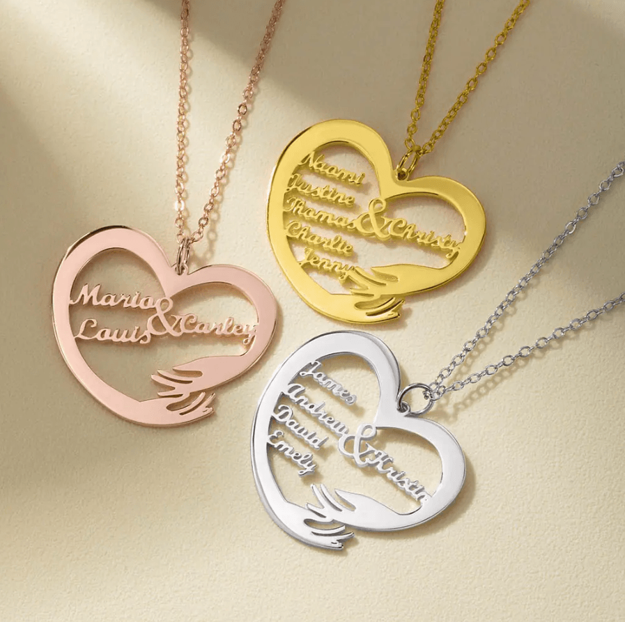 Three heart-shaped necklaces in gold, silver, and rose gold, each engraved with different names, arranged on a light-colored surface.