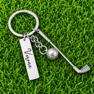 Custom name golf keychain with miniature golf club and ball charms displayed on green grass