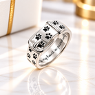 Personalized 925 sterling silver pet paw print buckle ring featuring black paw print details and an engraved message inside the band, displayed on an elegant white marble background with gold accents.