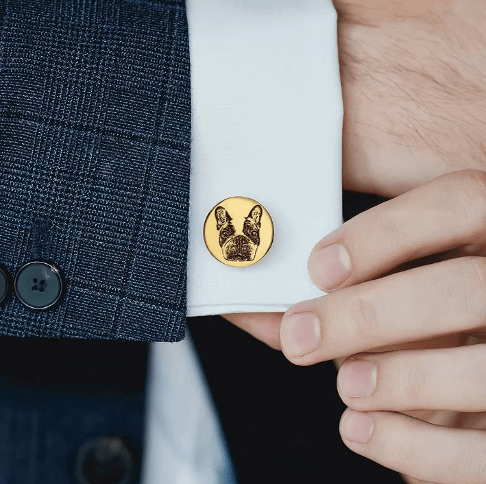 Gold cufflink with engraved French Bulldog portrait worn on a white shirt sleeve with a navy blue suit jacket.