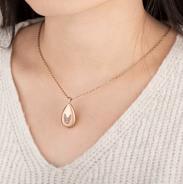 Rose gold teardrop pendant necklace featuring an engraved cat face, worn by a woman with a v-neck sweater.