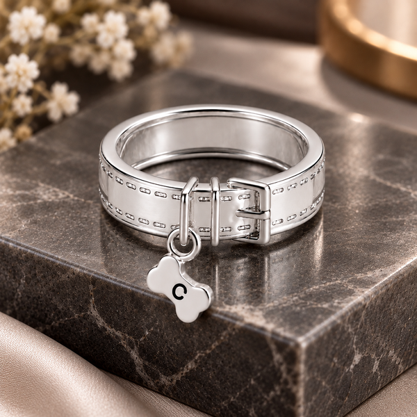 Personalized silver pet collar ring with buckle design and engraved bone charm featuring the letter C, displayed on a dark marble stand.