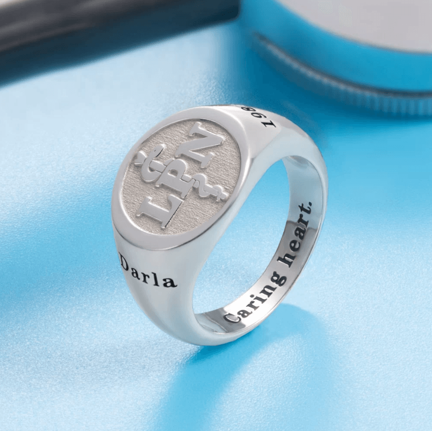 Silver ring with an engraved medical symbol (LPN) and the name "Darla." The inside of the band is inscribed with the phrase "Caring heart."