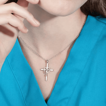 Silver cross necklace with stethoscope design and engraved name 'Claire', adorned with a birthstone, worn by a woman in a teal top.