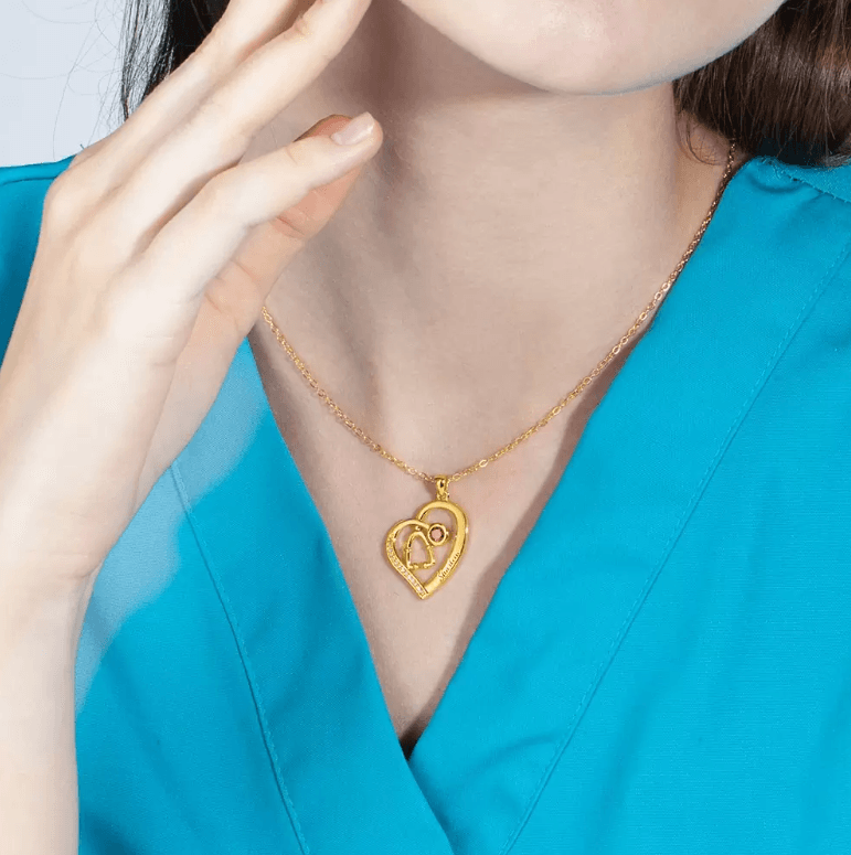 Gold heart-shaped pendant with stethoscope design and letter 'D' charm, on a woman in a teal blouse.