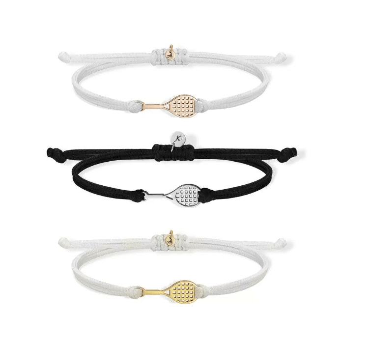 Three cord bracelets, two white and one black, each featuring a tennis racket charm in gold, silver, and rose gold, arranged in a vertical row.