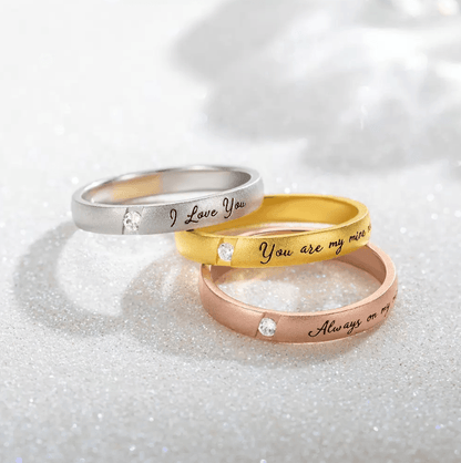 Three stacked rings in silver, gold, and rose gold, each engraved with romantic phrases and embedded with diamonds