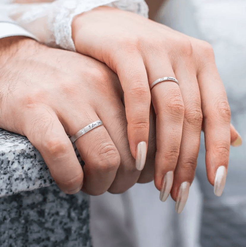 Close-up of a couple's hands clasped together, showing silver wedding bands engraved with romantic vows.