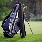 A sleek golf bag, featuring a black and silver design with convenient pockets and a set of clubs, stands on a grassy field with a personalized, insulated black beer can bag with the red initials 'YC' attached to it. The beer can bag is designed for easy transportation on the golf course, complementing the golf bag's professional look.