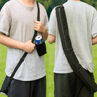 A dual image of a person wearing a grey t-shirt and black shorts, carrying a black insulated beer can bag with an adjustable shoulder strap. On the left, the person is holding a can in a black koozie with their right hand. On the right, the person is shown from the back, with the beer can bag resting comfortably along their side. The setting appears to be a lush green lawn, typically found at a golf course.