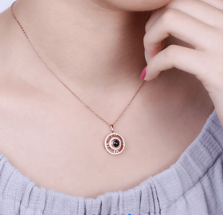 Close-up of a person wearing a rose gold pendant with a black gemstone and Roman numerals, highlighting the intricate design on a delicate chain.