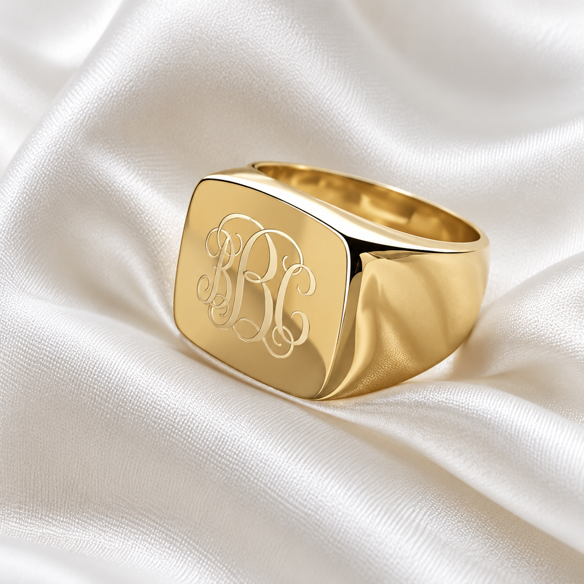 Personalised gold square signet ring with engraved monogram initials displayed on elegant white satin.