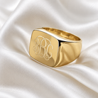 Personalised gold square signet ring with engraved monogram initials displayed on elegant white satin.