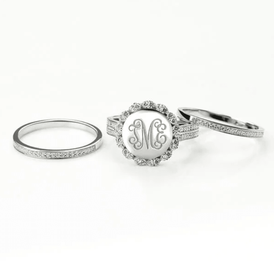 Three sterling silver rings with a central one featuring a monogram "TME" within a scalloped edge, surrounded by cubic zirconia, against a white background.