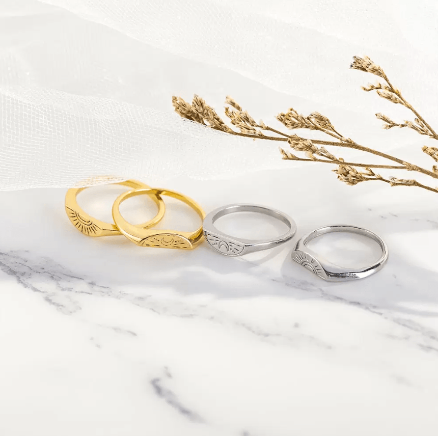 Gold and silver sun and moon rings displayed elegantly with dried flowers on a marble surface.