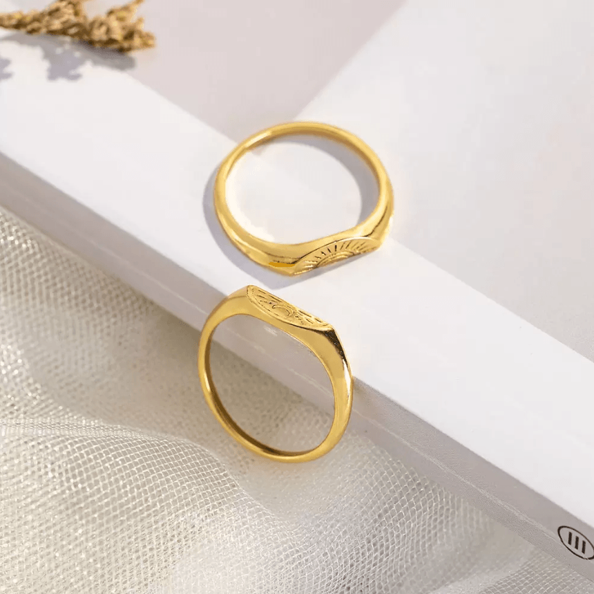 Gold and silver ring sets with sun and moon motifs, alongside dried wheat on marble.