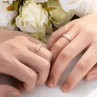 Hands with gold sun and moon rings touch gently against a backdrop of white roses.