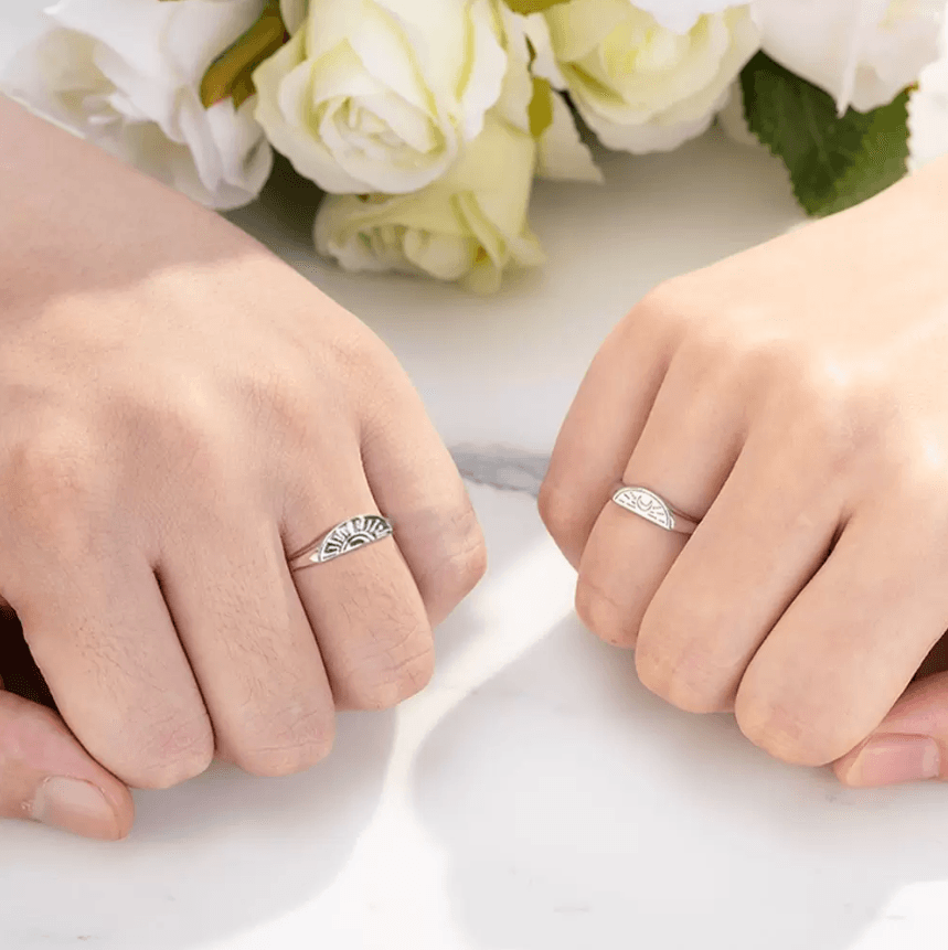 Two hands with silver sun and moon rings clasped together beside soft white blooms.