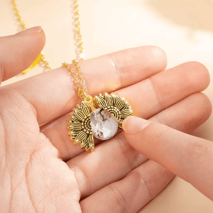 Hand holding a gold sunflower locket with a personalized photo insert on a chain.