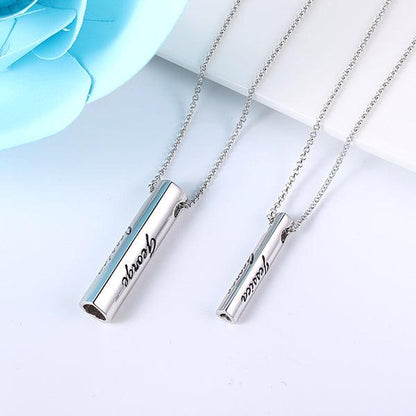 Two personalized sterling silver bar pendant necklaces with "Jessica" and "George" engravings, displayed on a white surface with a blue flower accent.