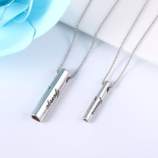Two personalized sterling silver bar pendant necklaces with "Jessica" and "George" engravings, displayed on a white surface with a blue flower accent.