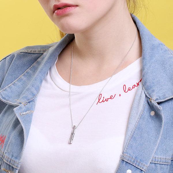 Woman wearing a personalized sterling silver bar pendant necklace, engraved with names, paired with a white t-shirt and denim jacket.