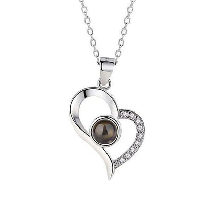 A silver heart-shaped pendant necklace with a central black gemstone and small clear crystals on one side of the heart.