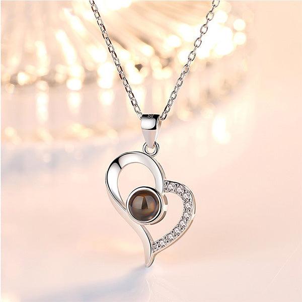Elegant silver heart-shaped pendant necklace featuring a central black gemstone and small clear crystals on one side, with a soft-focus background.