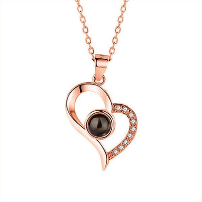 Rose gold heart-shaped pendant necklace featuring a central black gemstone and small clear crystals on one side, with a matching rose gold chain.