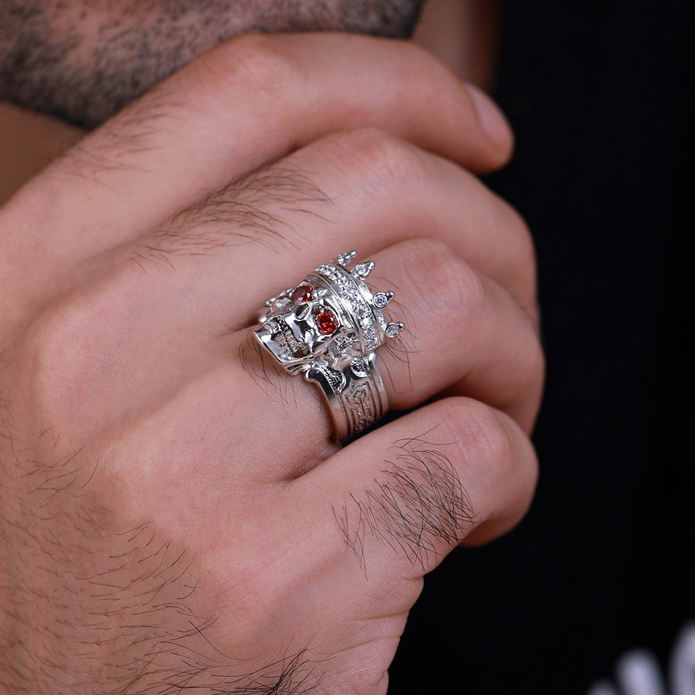 Close-up of a silver skull king ring with red gems and crown on a man's finger.