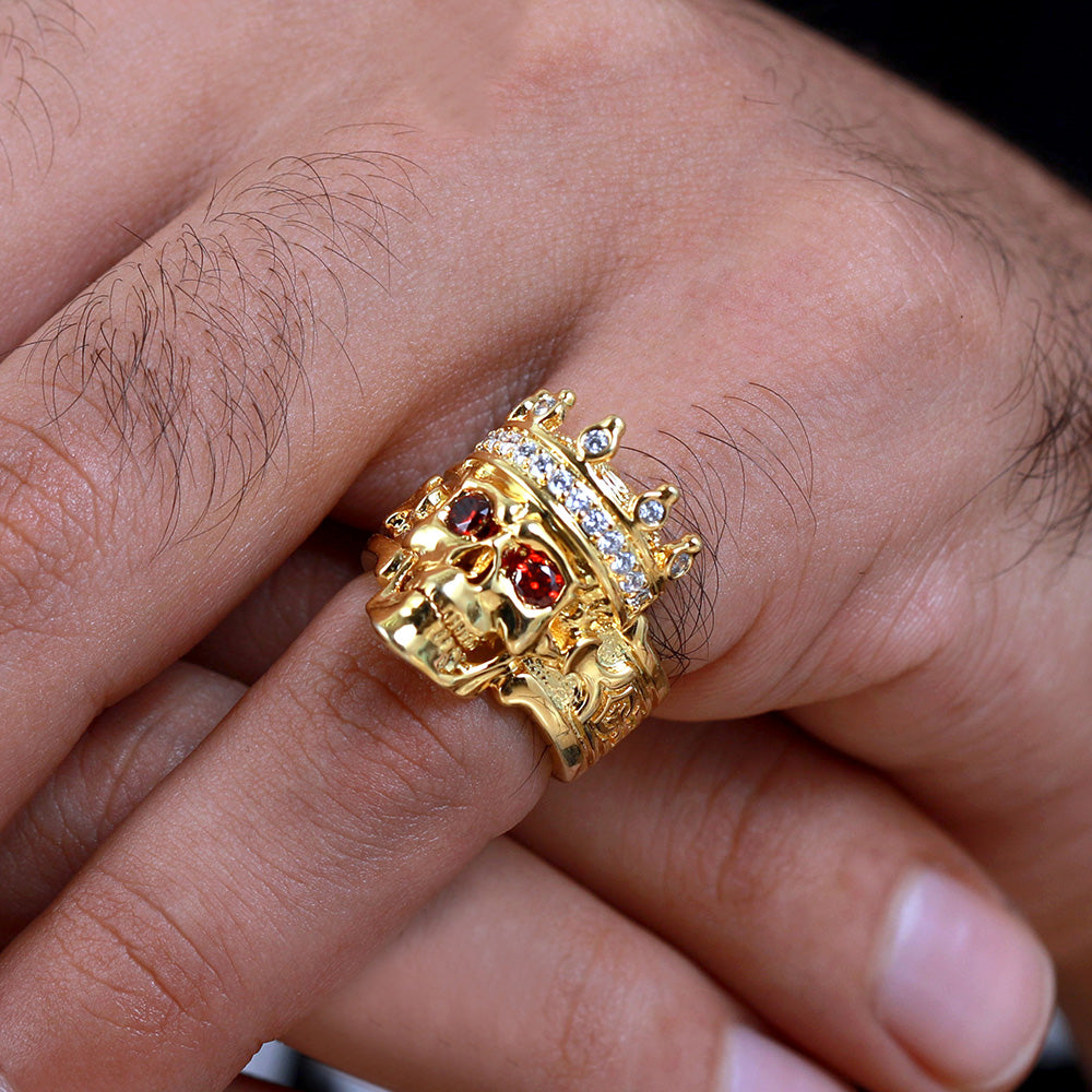 Hand wearing a golden skull king ring with red eyes and diamond crown detail.