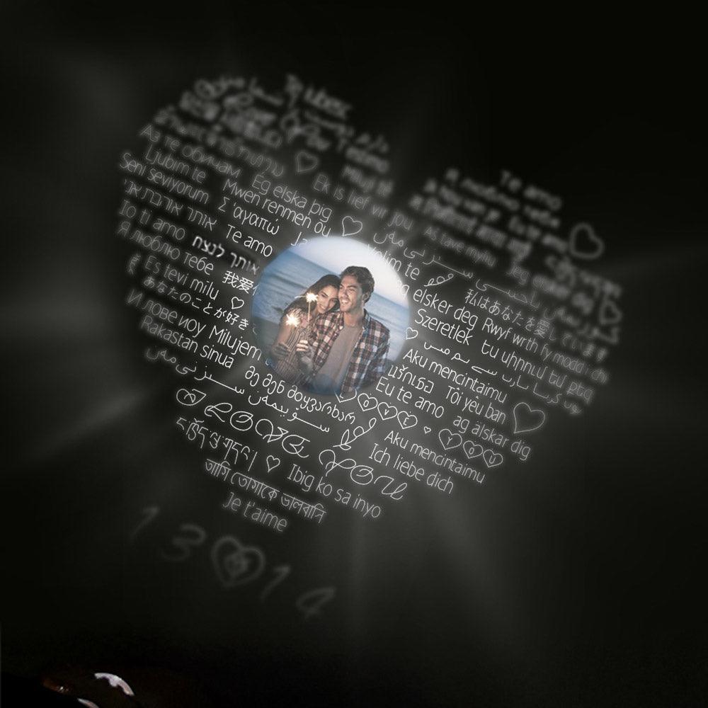 Heart-shaped projection with "I love you" in multiple languages surrounding a central photo of a couple, illuminated against a dark background.