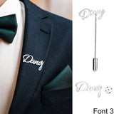 Suit with 'Dany' silver script lapel pin, white shirt, and green tie and pocket square.