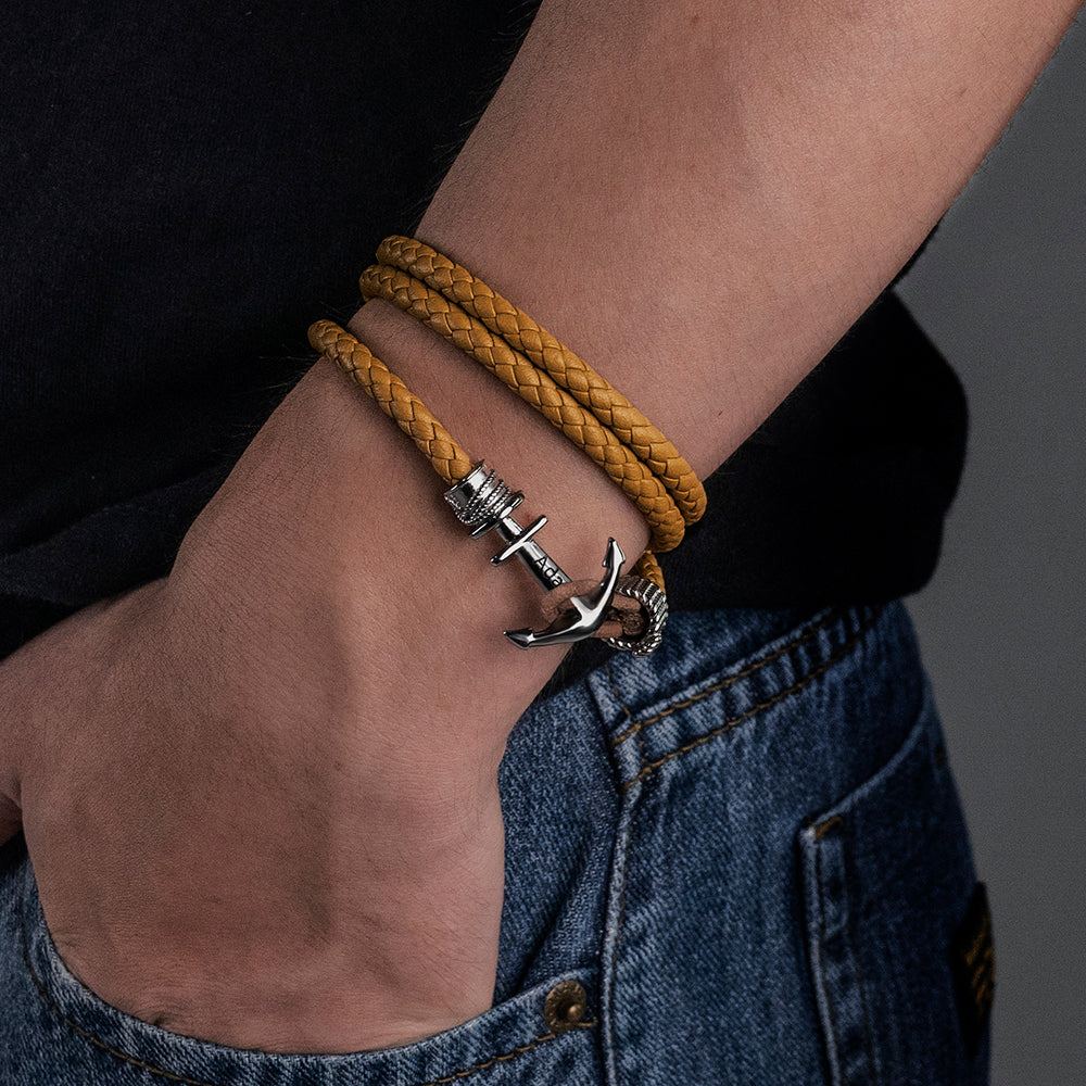 Person wearing a yellow braided leather bracelet with a silver anchor clasp against a denim backdrop.