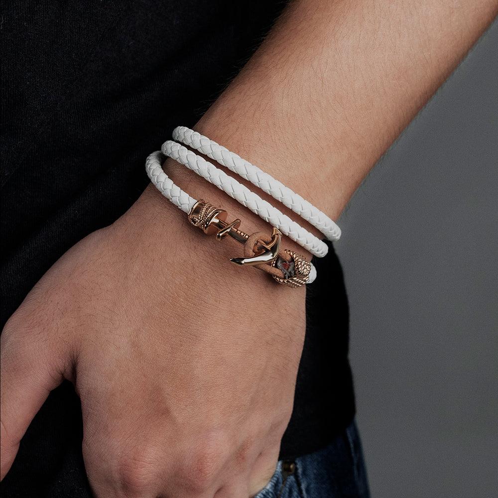 Person wearing a white braided bracelet with a rose gold anchor clasp.