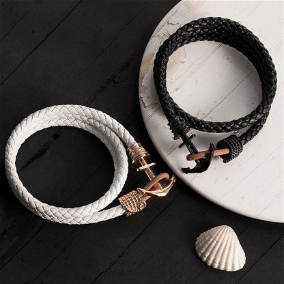 White and black braided bracelets with rose gold and black anchor clasps on a rustic surface.