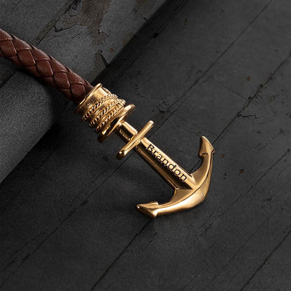 A golden anchor bracelet with the name "Brandon" on a black textured surface.